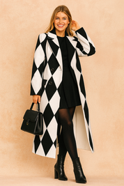 Black and white harlequin-patterned long coat, styled with a black mini dress, sheer tights, ankle boots, and a structured handbag.