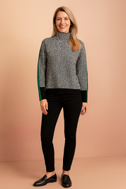 Black and white herringbone patterned high-neck sweater with green side stripes, black hem, and matching black cuffs, paired with slim-fit black trousers and black loafers.
