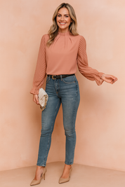 High-neck blouse with sheer chevron sleeves, pleated front, and a tailored fit paired with high-waisted jeans.
