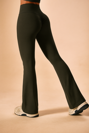 High-waisted dark olive green flared workout pants with ruched back seam and sleek silhouette, styled with athletic sneakers.