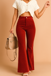 High-waisted burnt red corduroy flared pants styled with a cropped knit button-up top and beige heeled sandals, paired with a nude suede handbag.