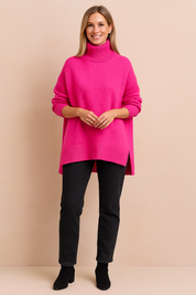 Hot pink oversized knit turtleneck sweater with ribbed hem and high collar, paired with slim-fit black pants and ankle boots.