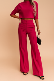 High-waisted hot pink tailored wide-leg trousers with structured seams and belt loops, paired with a matching cropped short-sleeve top made from a textured fabric.