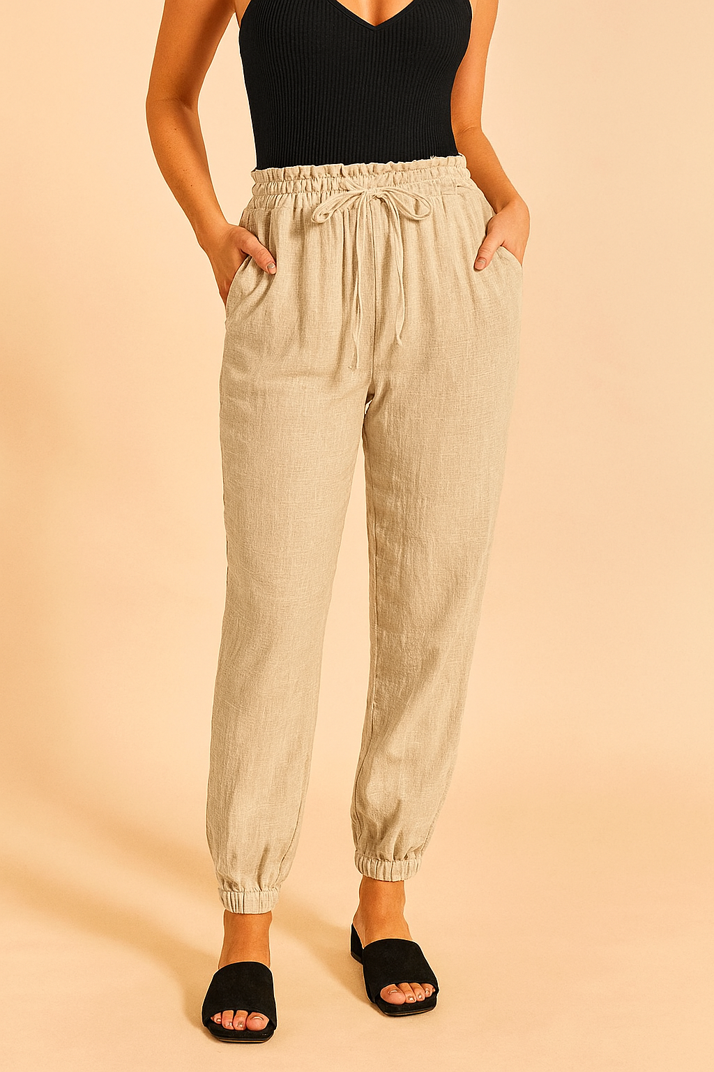 High-waisted beige drawstring jogger pants with a grid-textured finish, featuring an elastic waistband and ankle cuffs, styled with side pockets and a relaxed fit.