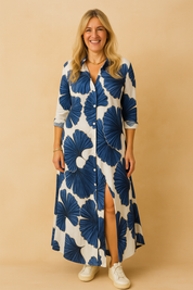 White button-down maxi dress with blue fan-shaped leaf print, featuring a front slit and three-quarter sleeves.