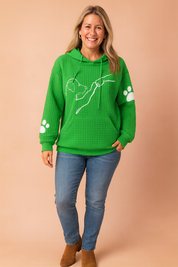 Green waffle-knit hoodie with front kangaroo pocket, featuring a white line art print of a dog reaching for a hand on the chest and white paw prints on each sleeve.