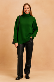 Forest green oversized turtleneck sweater in soft knit fabric with ribbed edges, styled with black leather-look pants and black loafers, paired with a sleek black shoulder bag.