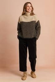 Cozy two-tone turtleneck sweater with a soft beige top section and black herringbone patterned lower half, paired with relaxed black corduroy pants and beige lace-up ankle boots.