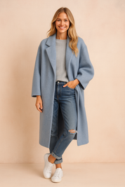 Light blue oversized long coat with relaxed sleeves and notched lapel, styled over a ribbed gray sweater, distressed jeans, and white sneakers.