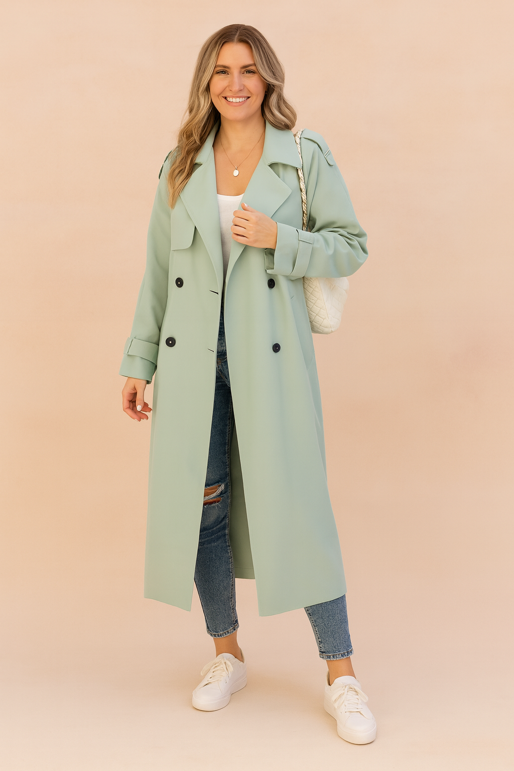 Mint green double-breasted trench coat with black buttons, paired with a white top, distressed blue skinny jeans, and white lace-up sneakers.