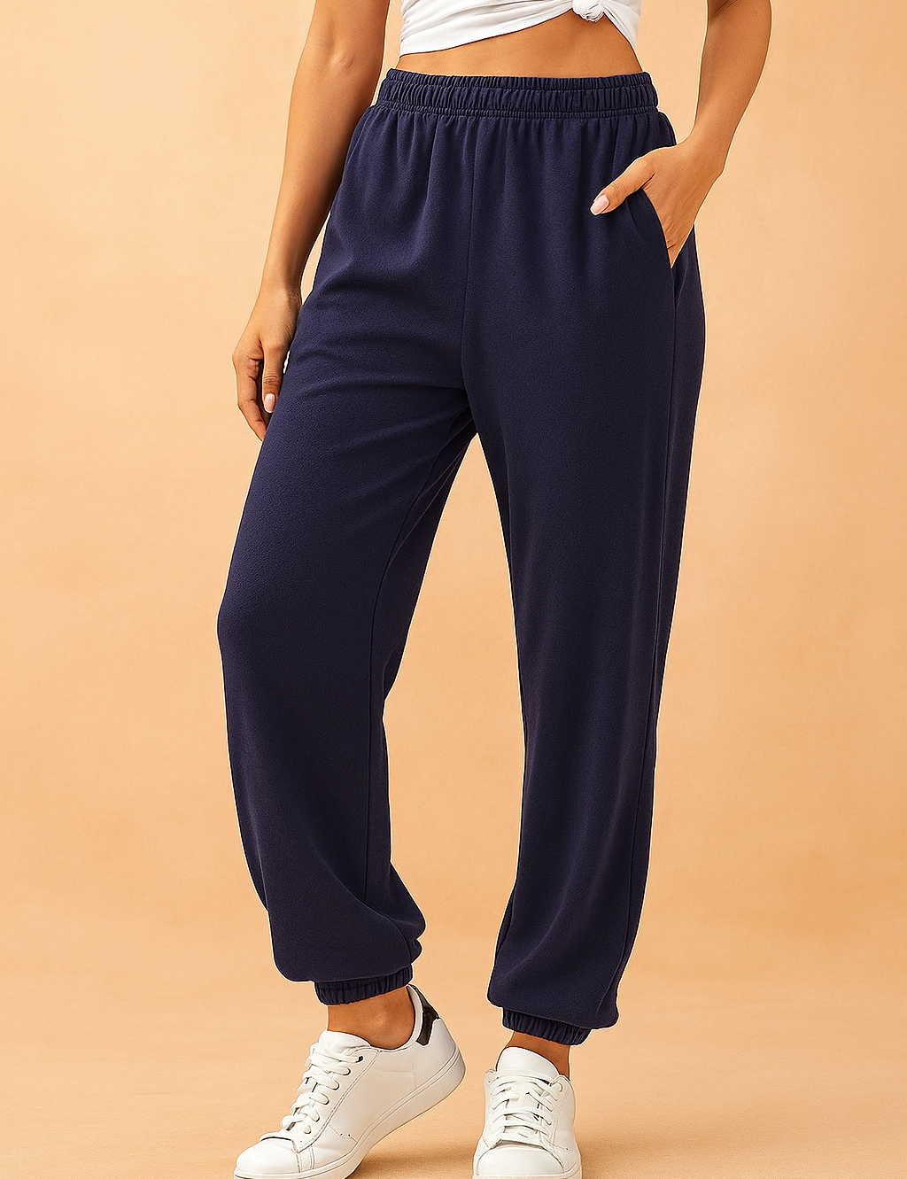 Navy blue tapered sweatpants with elastic waistband and ankle cuffs, styled casually with a white crop top and white sneakers.
