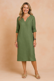 Minimalist olive green linen shift dress with V-neckline and 3/4 roll-tab sleeves, styled with neutral sandals and a relaxed silhouette, perfect for summer casual wear.