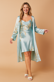 Two-piece satin lounge set featuring a cowl neck mini slip dress and matching long robe, both in pastel blue with delicate golden blossom print, styled with soft drape and subtle sheen.
