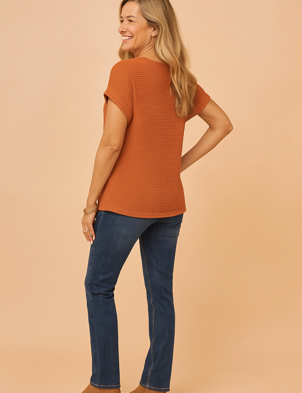 Textured rust-orange waffle knit short-sleeve blouse with rolled cuffs, styled with dark blue slim-fit jeans and tan ankle boots.