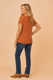 Textured rust-orange waffle knit short-sleeve blouse with rolled cuffs, styled with dark blue slim-fit jeans and tan ankle boots.