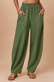 Wide-leg sage green linen pants with an elastic waistband and large front patch pockets, styled with flat tan sandals and a cropped beige top.