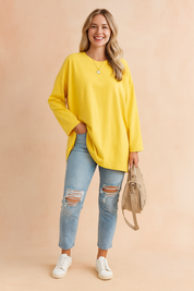 Bright yellow oversized long-sleeve tunic top paired with light blue distressed skinny jeans, styled with a beige handbag and white sneakers.