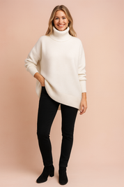Ivory white oversized knit turtleneck sweater with ribbed cuffs and hem, paired with black slim-fit trousers and ankle boots.