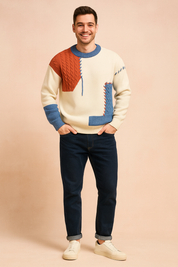 Color-block knit sweater featuring a cream base with textured cable-knit red and diamond-patterned blue panels, finished with blue and red whipstitch accents and ribbed hems for a bold, modern look.