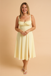 Ruched bust midi dress with structured bodice, wide shoulder straps, high slit detail, and flared hemline in soft lemon yellow.