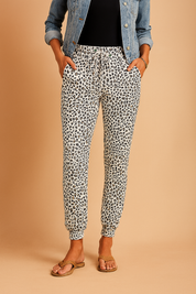 White jogger pants with a bold black and gray leopard print, featuring a drawstring waist, cuffed ankles, and a relaxed tapered fit.
