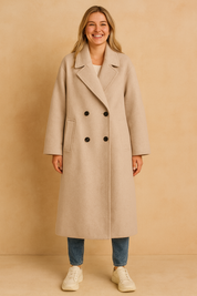 Light beige double-breasted long coat with black buttons, wide lapel collar, and side pockets, styled with jeans and sneakers for a modern casual look.
