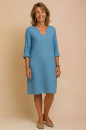 Relaxed-fit light blue linen V-neck shift dress with 3/4 rolled sleeves and minimal seams, styled for casual elegance with clean lines and above-the-knee length.