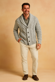 Light gray cable knit cardigan with shawl collar, button closure, layered over an olive-gray shirt, paired with off-white trousers and brown leather shoes
