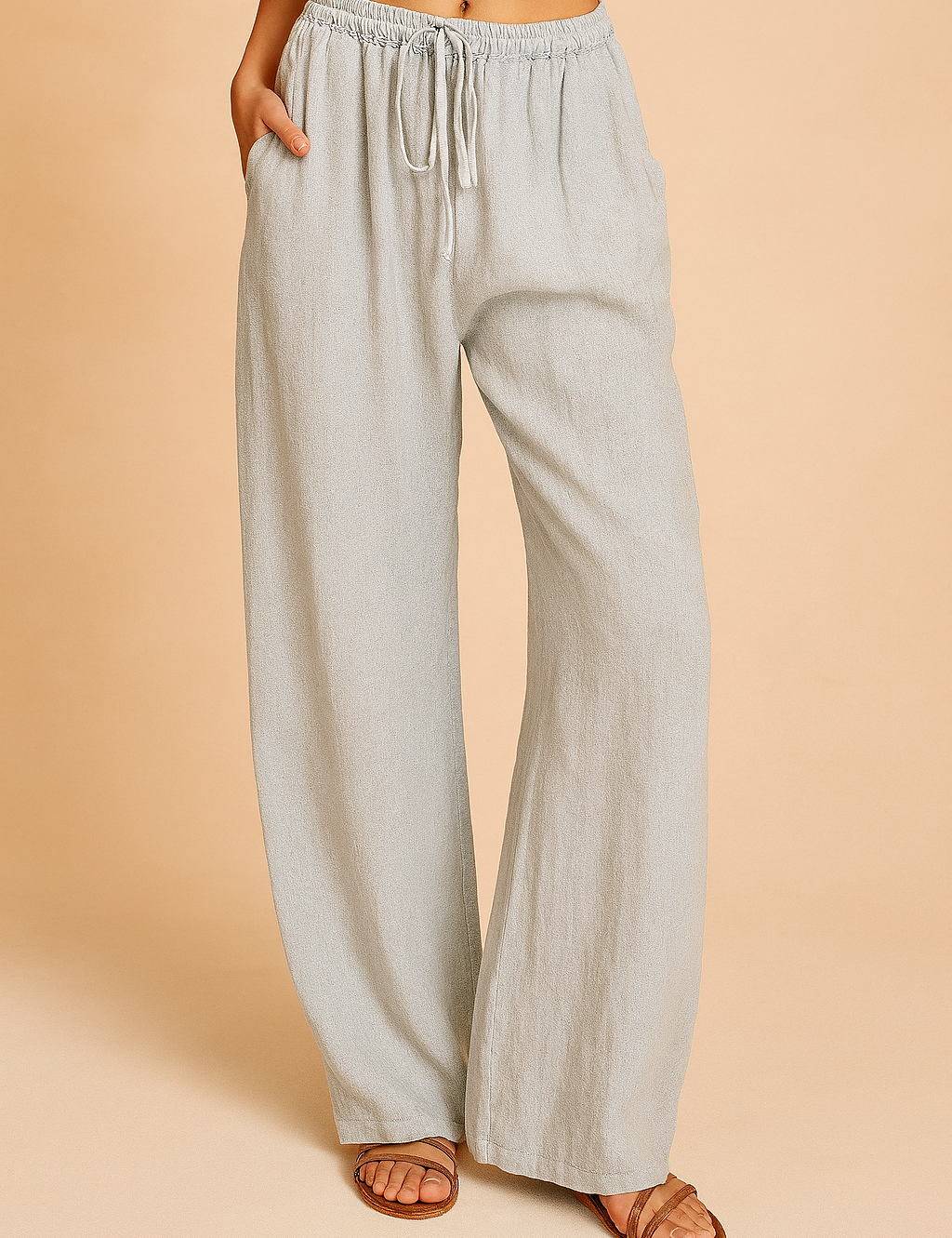 Light gray linen wide-leg pants with a drawstring waist, subtle natural weave texture, and side pockets, styled with brown leather sandals.
