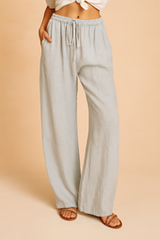 Light gray linen wide-leg pants with a drawstring waist, subtle natural weave texture, and side pockets, styled with brown leather sandals.