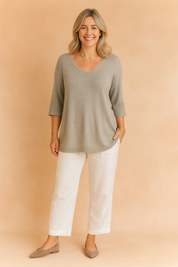 Light grey V-neck knit tunic with three-quarter sleeves, paired with white straight-leg linen trousers and taupe flats.