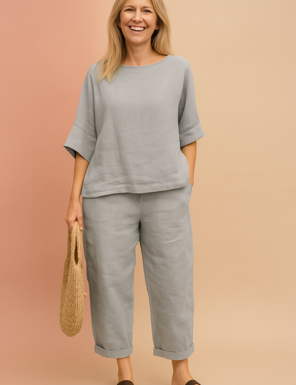 Two-piece light grey linen set with loose half-sleeve top and relaxed ankle-length pants, styled with a rolled hem and matched with brown flat sandals and a woven straw bag.