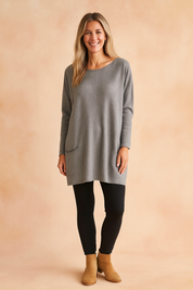 Light grey oversized knit tunic sweater with long sleeves, single front patch pocket, soft texture, and relaxed fit, paired with black leggings and tan suede ankle boots.Light grey oversized knit tunic sweater with long sleeves, single front patch pocket, soft texture, and relaxed fit, paired with black leggings and tan suede ankle boots.