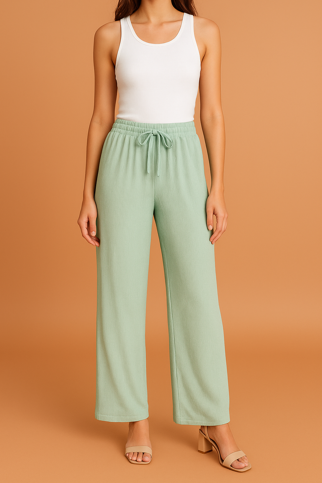 Light sage green wide-leg pleated pants with a ribbed texture and drawstring waistband, styled with a white tank top and nude block-heeled sandals.