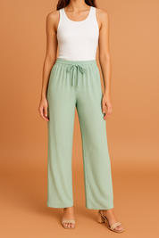 Light sage green wide-leg pleated pants with a ribbed texture and drawstring waistband, styled with a white tank top and nude block-heeled sandals.