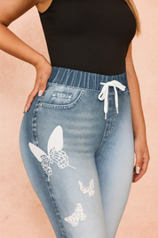 Light blue high-waist jeggings with butterfly print and drawstring waist, styled with a ribbed sleeveless black crop top for a casual chic look
