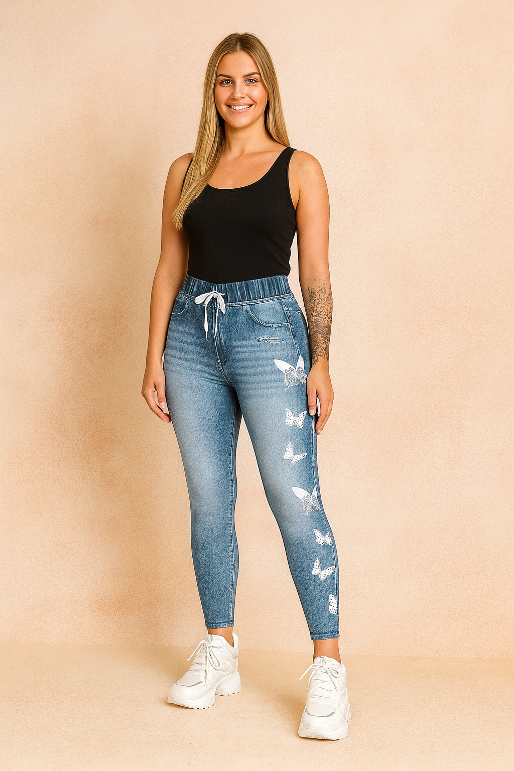 Light blue high-waist jeggings with white butterfly prints and drawstring waist, styled with a sleeveless black top and chunky white sneakers.