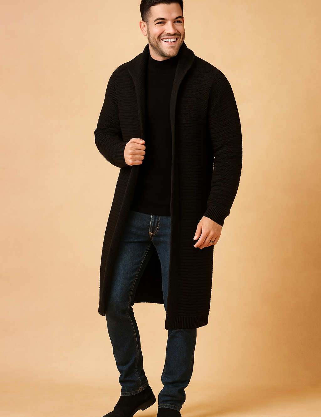 Long black ribbed knit cardigan for men, styled with a fitted black sweater, slim blue jeans, and black suede Chelsea boots.