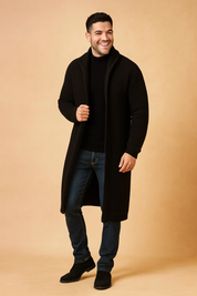Long black ribbed knit cardigan for men, styled with a fitted black sweater, slim blue jeans, and black suede Chelsea boots.