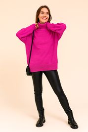Vibrant magenta oversized knit turtleneck sweater paired with black faux leather leggings, styled with black ankle boots and a minimalist shoulder bag