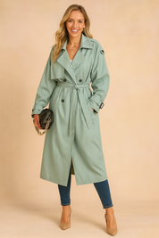 Mint green double-breasted trench coat with waist belt, epaulets, and side pockets styled with skinny jeans and beige heels.