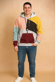 Multicolor patchwork hoodie with pastel yellow, pink, blue, burgundy, brown, and gray panels, featuring a kangaroo pocket and drawstrings, styled with jeans and white sneakers.