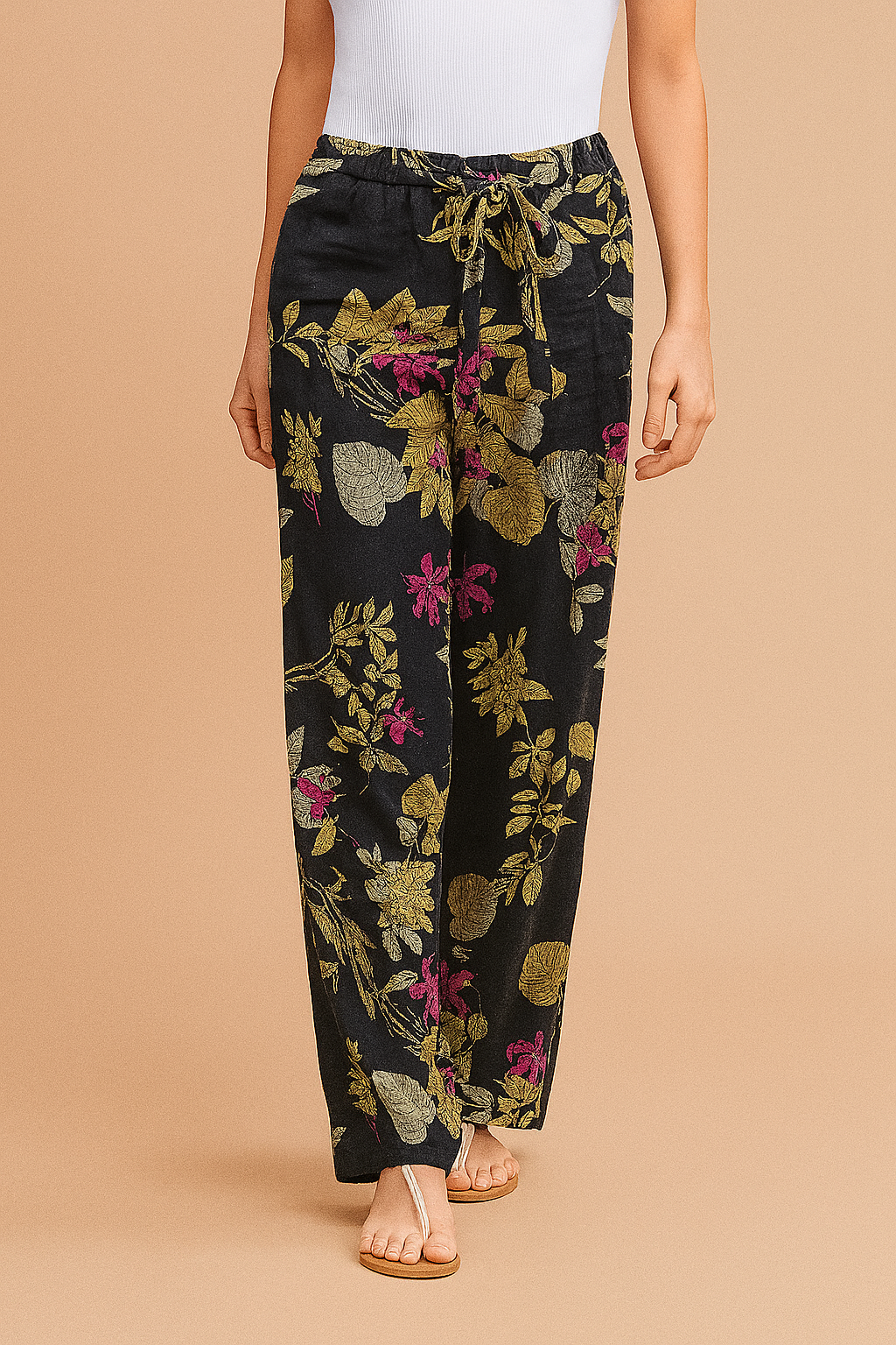 Wide-leg navy blue pants with a bold botanical floral print in green, pink, and beige, featuring a drawstring waist and relaxed fit, styled with beige thong sandals.