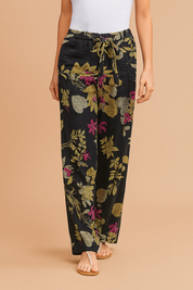 Wide-leg navy blue pants with a bold botanical floral print in green, pink, and beige, featuring a drawstring waist and relaxed fit, styled with beige thong sandals.