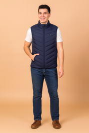 Men’s navy blue heated vest with chevron quilted design, full zip closure, and high collar. Paired with jeans and brown casual shoes for a modern, practical look