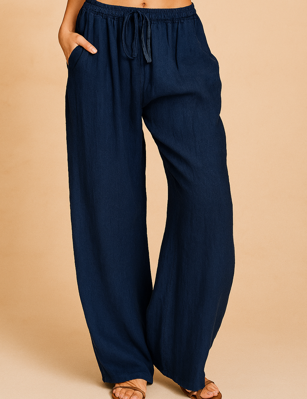 Navy blue wide-leg linen pants with an elastic drawstring waist, full-length drape, and a relaxed silhouette, styled with tan flat sandals.