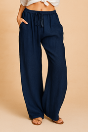 Navy blue wide-leg linen pants with an elastic drawstring waist, full-length drape, and a relaxed silhouette, styled with tan flat sandals.