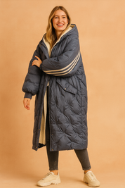 Navy blue quilted puffer coat with striped sleeve accents and faux shearling lining, styled with dark jeans and white sneakers for a cozy winter look.