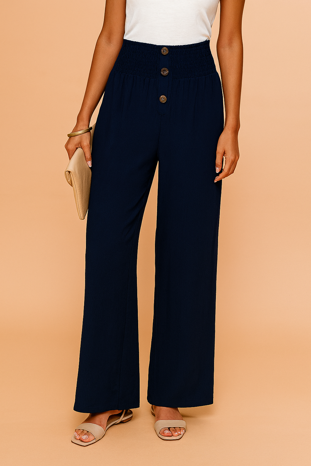 High-waisted navy wide-leg pants with a smocked waistband and three central buttons, styled with beige open-toe sandals and a neutral clutch.