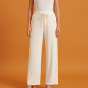 Off-white pleated wide-leg pants with a ribbed texture and drawstring waistband, styled with a white tank top and nude heels.